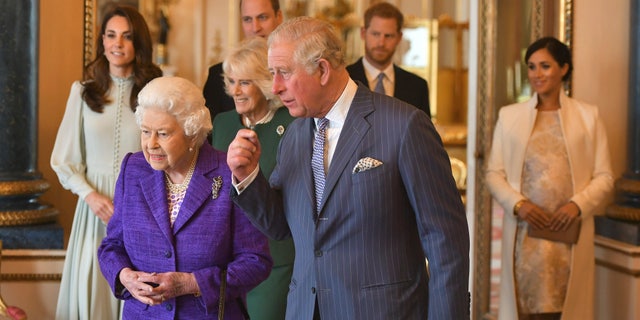 In this March 5, 2019 file photo, Britain's Queen Elizabeth II is joined by Prince Charles, the Prince of Wales, and at rear, from left, Kate, Duchess of Cambridge, Camilla, Duchess of Cornwall, Prince William, Prince Harry and Meghan, Duchess of Sussex during a reception at Buckingham Palace, London to mark the 50th anniversary of the investiture of the Prince of Wales. 