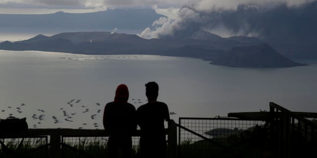 Men watch from Tagaytay, Cavite province, south of Manila, as Taal Volcano continues to spew ash on Tuesday, Jan. 14, 2020. Thousands of people fled the area through heavy ash as experts warned that the eruption could get worse and plans were being made to evacuate more.(AP Photo/Aaron Favila)