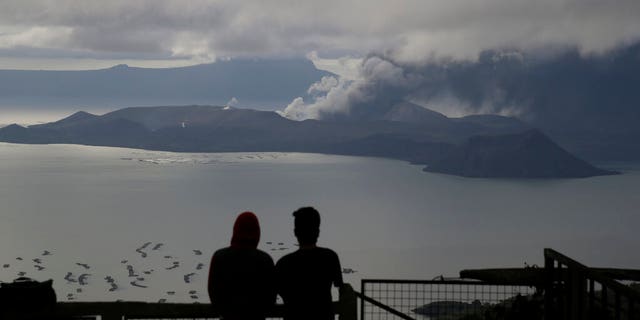 Men watch from Tagaytay, Cavite province, south of Manila, as Taal Volcano continues to spew ash on Tuesday, Jan. 14, 2020. Thousands of people fled the area through heavy ash as experts warned that the eruption could get worse and plans were being made to evacuate more.(AP Photo/Aaron Favila)