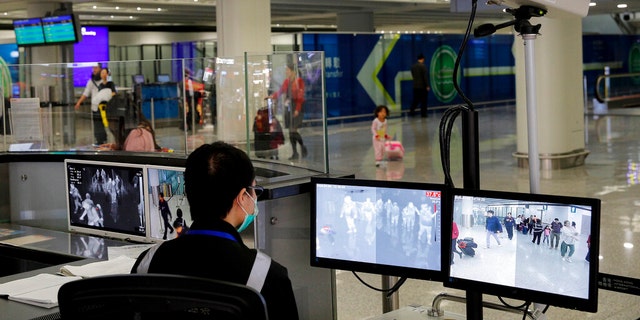 FILE - In this Jan. 4, 2020, file photo, a health surveillance officer monitors passengers arriving at the Hong Kong International airport in Hong Kong. On Friday, Jan. 17, 2020, the U.S. Centers for Disease Control and Prevention officials said they will begin screening airline passengers at three U.S. airports who traveled from Wuhan in central China, for a new illness that has prompted worries about a new international outbreak. (AP Photo/Andy Wong, File)