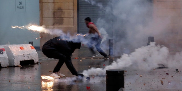 A protester throws back tear gas canister that was fired towards them by Lebanese riot police during an anti-government protest at a road leading to the parliament building in Beirut, Lebanon, Saturday, Jan. 18, 2020. Riot police fired tears gas and sprayed protesters with water cannons near parliament building to disperse thousands of people after riots broke out during a march against the ruling elite amid a severe economic crisis. (AP Photo/Hassan Ammar)