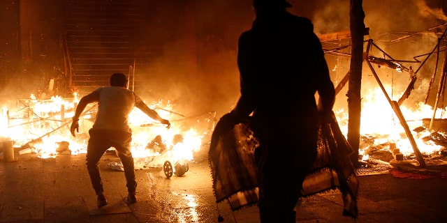 An anti-government protesters try to extinguish a gas cylinder and protesters tents, which set on fire by civilian men believed to be the private unit of the parliament guards, during ongoing protests against the political elites who have ruled the country since decades, in Beirut, Lebanon, Saturday, Jan. 18, 2020. Riot police fired tear gas and sprayed water cannon near parliament in Lebanon's capital Saturday to disperse thousands of protesters after riots broke out during a march against the ruling elite amid a severe economic crisis. (AP Photo/Hussein Malla)