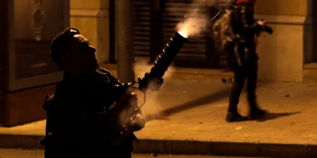A Riot police officer fires tear gas against anti-government protesters trying to enter parliament square during a protest at a road leading to the parliament building in Beirut, Lebanon, Saturday, Jan. 18, 2020. Riot police fired tears gas and sprayed protesters with water cannons near parliament building to disperse thousands of people after riots broke out during a march against the ruling elite amid a severe economic crisis. (AP Photo/Hassan Ammar)