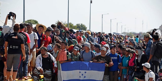 Central American migrants holding Honduras' national flag stand on the legal border crossing bridge over the Suchiate River that connects Tecun Uman, Guatemala with Ciudad Hidalgo in Mexico. (AP Photo/Moises Castillo)