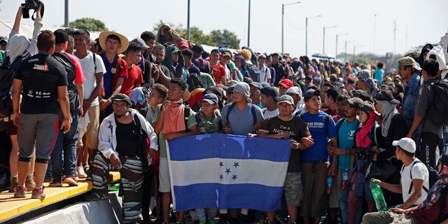 Central American migrants holding Honduras' national flag stand on the legal border crossing bridge over the Suchiate River that connects Tecun Uman, Guatemala with Ciudad Hidalgo in Mexico. (AP Photo/Moises Castillo)