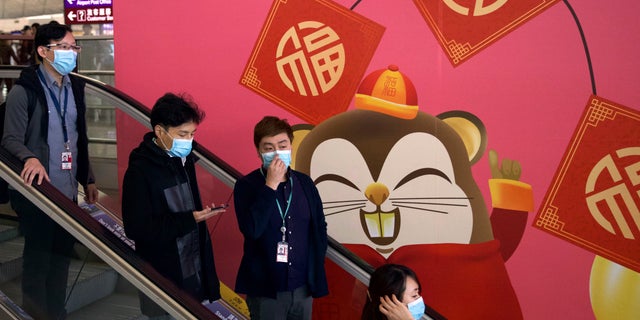 People wear face masks as they ride an escalator at the Hong Kong International Airport in Hong Kong, Tuesday, Jan. 21, 2020. Face masks sold out and temperature checks at airports and train stations became the new norm as China strove Tuesday to control the outbreak of a new coronavirus that has reached four other countries and territories and threatens to spread further during the Lunar New Year travel rush. (AP Photo/Ng Han Guan)