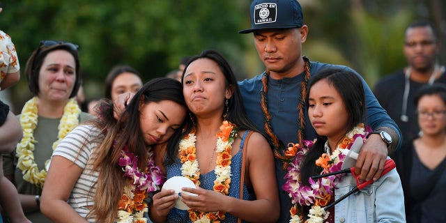 In this Tuesday, Jan. 21, 2020, photo, John Enriquez, center right, ex-husband of Honolulu Police Officer Tiffany Enriquez, holds their daughters Teiya Enriquez Sandoval, from bottom left, Jazzy and Triniti during a candlelight vigil in remembrance of Tiffany Enriquez in Honolulu. A handyman's landlord had recently started an eviction process before he stabbed a woman Sunday and fatally shot two Honolulu officers, including Enriquez. (Bruce Asato/Honolulu Star-Advertiser via AP)