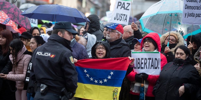 A woman holds a Venezuelan flag as others pack the Puerta del Sol square waiting for Juan Guaido during his visit to Madrid, Spain, Saturday, Jan. 25, 2020. Juan Guaido, the man who one year ago launched a bid to oust Venezuelan President Nicolas Maduro, arrived Saturday in Spain, where a thriving community of Venezuelans and a storm among Spanish political parties awaited him. Banners read 'Peace and6Freedom' (AP Photo/Paul White)