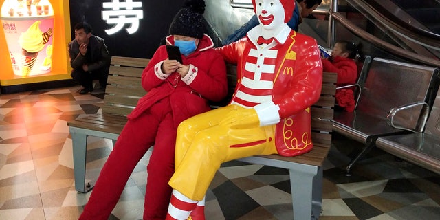 A woman wears a face mask and she uses her smartphone as she sits next to a statue of Ronald McDonald at a McDonald's restaurant in Suzhou in eastern China's Jiangsu Province on Jan. 26. (Chinatopix via AP)
