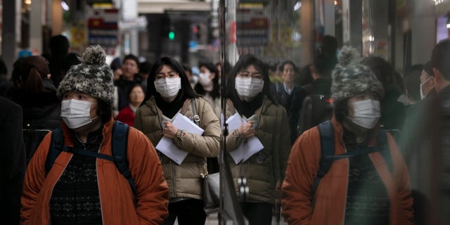 Commuters wearing protective face masks walk on a sidewalk Monday, Jan. 27, 2020, in the Shinjuku district of Tokyo. China has extended its Lunar New Year holiday three more days to discourage people from traveling as it tries to contain the spread of a viral illness that has caused dozens of deaths. (AP Photo/Jae C. Hong)