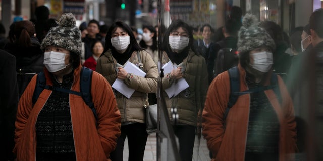 Commuters wearing protective face masks walk on a sidewalk Monday, Jan. 27, 2020, in the Shinjuku district of Tokyo. China has extended its Lunar New Year holiday three more days to discourage people from traveling as it tries to contain the spread of a viral illness that has caused dozens of deaths. (AP Photo/Jae C. Hong)