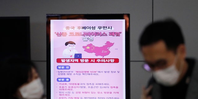 A poster warning about coronavirus is seen as passengers wear masks in a departure lobby at Incheon International Airport in Incheon, South Korea, Monday, Jan. 27, 2020. China on Monday expanded sweeping efforts to contain a viral disease by extending the Lunar New Year holiday to keep the public at home and avoid spreading infection. The sign reads " A new coronavirus occurs in Wuhan City, China." (AP Photo/Ahn Young-joon)