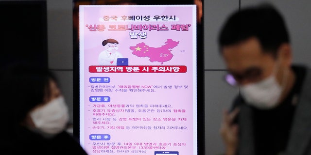 A poster warning about coronavirus is seen as passengers wear masks in a departure lobby at Incheon International Airport in Incheon, South Korea, Monday, Jan. 27, 2020. China on Monday expanded sweeping efforts to contain a viral disease by extending the Lunar New Year holiday to keep the public at home and avoid spreading infection. The sign reads 