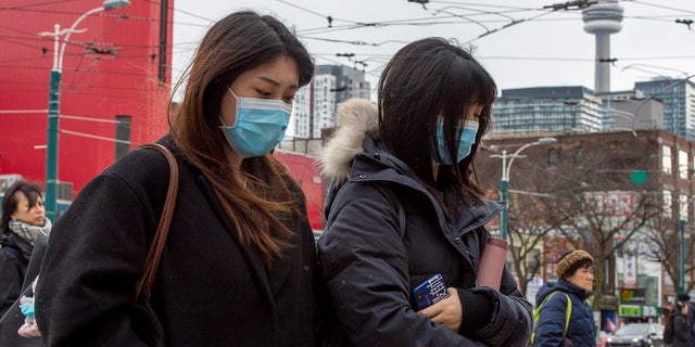 Pedestrians wear protective masks as they walk in Toronto on Monday. Canada's first presumptive case of the novel coronavirus has been officially confirmed, Ontario health officials said Monday as they announced the patient's wife has also contracted the illness. Surgical-style masks at U.S. pharmacies have reportedly begun selling out in several cities amid fears of the virus. (Frank Gunn/The Canadian Press via AP)