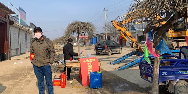 A man wearing a face mask stands near a barricade at the entrance to Donggouhe village in northern China's Hebei Province on Wednesday. With barricades and wary guardians, villages on the outskirts of Beijing are closing themselves off to outsiders to ward against infection amid the outbreak of a new type of virus. (AP Photo)