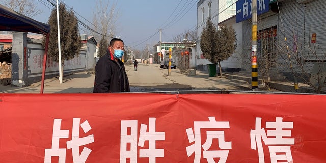 A man wearing a face mask stands near a banner reading 