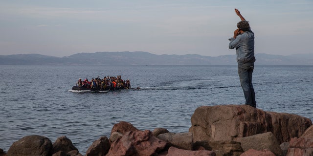 In this Wednesday, Sept. 9, 2015 photo refugees and migrants aboard an overcrowded dinghy as they cross the Aegean Sea, from Turkey, that is seen in the background, to the coast of Lesbos island, Greece. (AP Photo/Petros Giannakouris)