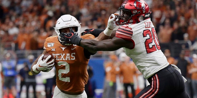 Texas running back Roschon Johnson (2) has his face mask grabbed by Utah linebacker Devin Lloyd (20) during the second half of the Alamo Bowl NCAA college football game in San Antonio, Tuesday, Dec. 31, 2019. (AP Photo/Eric Gay)
