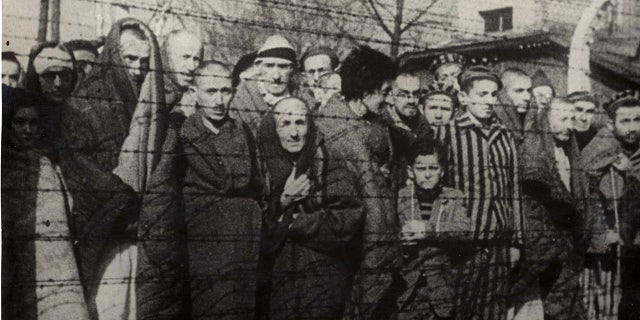 Holocaust survivors stand behind a barbed-wire fence after the liberation of Nazi German death camp Auschwitz-Birkenau in 1945 in Nazi-occupied Poland, in this handout picture obtained by Reuters on January 19, 2020. Courtesy of Yad Vashem Archives/Handout via REUTERS