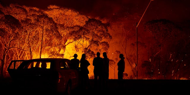 Residents look on as flames burn through bush on January 04, 2020 in Lake Tabourie, Australia. A state of emergency has been declared across NSW with dangerous fire conditions forecast for Saturday, as more than 140 bushfires continue to burn. There have been eight confirmed deaths in NSW since Monday 30 December. 1365 homes have been lost, while 3.6 million hectares have been burnt this fire season.