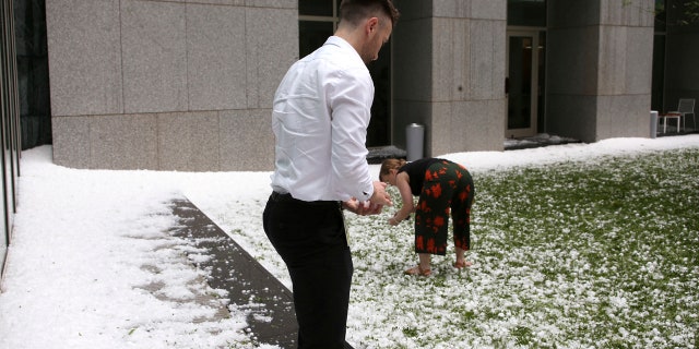 A man and woman collect golfball-sized hail on the grounds of Parliament House in Canberra, Australia, after a storm battered the Australian capital, Monday, Jan. 20, 2020.