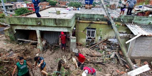 Locals work to clean up mud and debris around houses destroyed by a landslide after heavy rains in Vila Ideal neighborhood, Ibirite municipality, Minas Gerias state, Brazil.