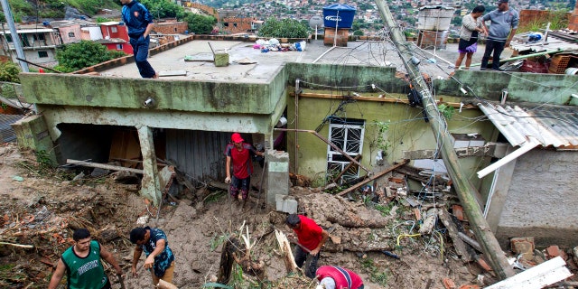 Locals work to clean up mud and debris around houses destroyed by a landslide after heavy rains in Vila Ideal neighborhood, Ibirite municipality, Minas Gerias state, Brazil.