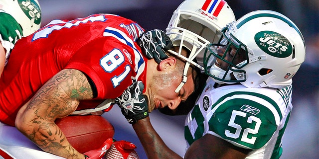 New England Patriots tight end Aaron Hernandez (81) hangs on to the ball as New York Jets inside linebacker David Harris (52) takes off his helmet on a hit during the first half of an NFL football game in Foxborough, Mass., Sunday, Oct. 9, 2011.
