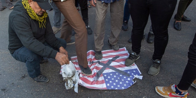Mourners step over a U.S. flag before burning it during the funeral of Iran's top general, Qassem Soleimani, and Abu Mahdi al-Muhandis, deputy commander of Iran-backed militias in Iraq known as the Popular Mobilization Forces, in Baghdad, Iraq, Saturday, Jan. 4, 2020. Thousands of mourners chanting "America is the Great Satan" marched in a funeral procession Saturday through Baghdad for Iran's top general and Iraqi militant leaders, who were killed in a U.S. airstrike. (AP Photo/Nasser Nasser)