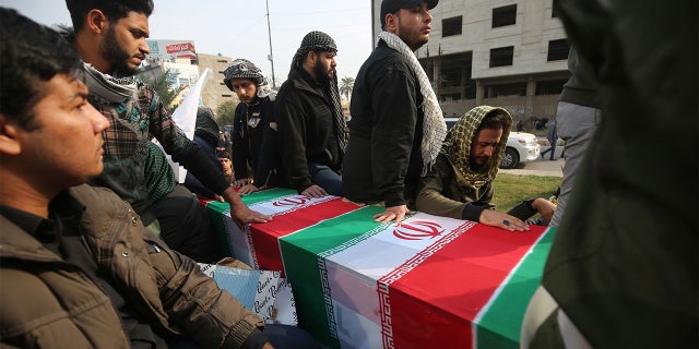Iraqis surround a coffin, draped in an Iranian national flag, during the funeral procession of Iraqi paramilitary chief Abu Mahdi al-Muhandis, Iranian military commander Qasem Soleimani, and eight others, in the capital Baghdad's district of al-Jadriya, near the high-security Green Zone, on January 4, 2020. - Thousands of Iraqis chanting
