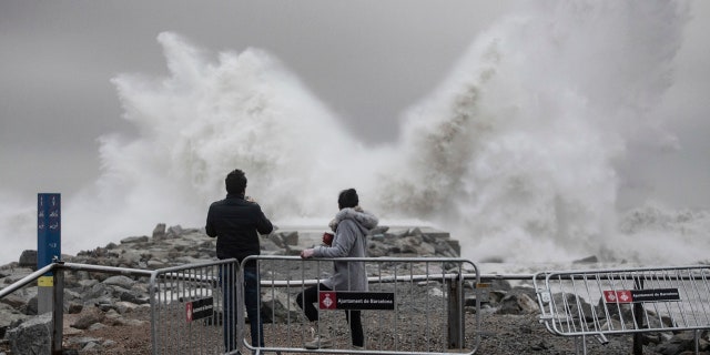 Two people watch the waves hitting the breakwater in Barcelona, Spain, Wednesday, Jan. 22, 2020.