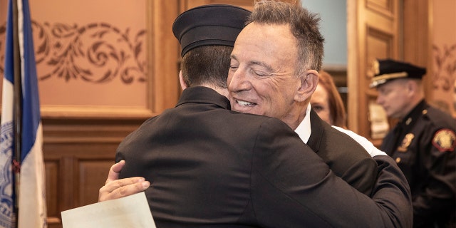 In this photo provided by the Jersey City Mayor's Office, Bruce Springsteen hugs his son Sam Springsteen after he is sworn in as a Jersey City Firefighter at City Hall in Jersey City, N.J. (Jennifer Brown/Jersey City Mayor's Office via AP)