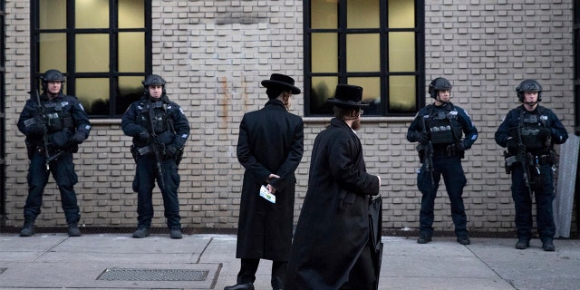 FILE - In this Dec. 11, 2019 file photo, Orthodox Jewish men pass New York City police guarding a Brooklyn synagogue prior to a funeral for Mosche Deutsch, a rabbinical student from Brooklyn who was killed in a shooting at a Jersey City, N.J. market. (AP Photo/Mark Lennihan, File)