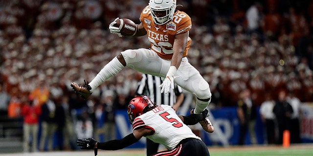 Texas running back Keaontay Ingram (26) leaps over Utah defensive back Tareke Lewis (5) during the second half of the Alamo Bowl NCAA college football game in San Antonio, Tuesday, Dec. 31, 2019. (AP Photo/Eric Gay)