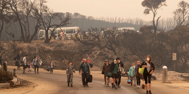 Evacuees walk down to the beach to board vessels and be ferried out to the navy's HMAS Choules, Friday, Jan. 3, 2020, in Mallacoota, Victoria, Australia.