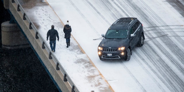Snow accumulates as pedestrians walk on East State Street, on Saturday, Jan. 11, 2020, in Rockford, Ill.