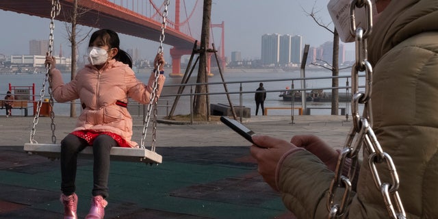 A girl wears a face mask as she play on a swing near the Yingwuzhou Yangtze River Bridge in Wuhan in central China's Hubei Province, Wednesday, Jan. 29, 2020. Countries began evacuating their citizens Wednesday from the Chinese city hardest-hit by a new virus that has now infected more people in China than were sickened in the country by SARS. (AP Photo/Arek Rataj)