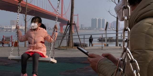 A girl wears a face mask as she play on a swing near the Yingwuzhou Yangtze River Bridge in Wuhan in central China's Hubei Province, Wednesday, Jan. 29, 2020. Countries began evacuating their citizens Wednesday from the Chinese city hardest-hit by a new virus that has now infected more people in China than were sickened in the country by SARS. (AP Photo/Arek Rataj)