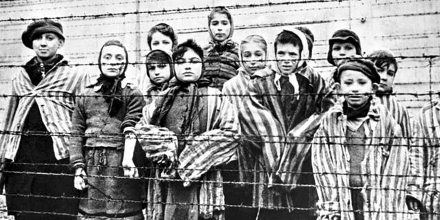 A group of child survivors behind a barbed wire fence at the Nazi concentration camp at Auschwitz-Birkenau in southern Poland, on the day of the camp’s liberation by the Red Army, 27th January 1945. Photo taken by Red Army photographer Captain Alexander Vorontsov during the making of a film about the liberation of the camp. The children were dressed in adult uniforms by the Russians. The children are (left to right): Tomy Schwarz (later Shacham), Miriam Ziegler, Paula Lebovics (front), Ruth Webber, Berta Weinhaber (later Bracha Katz), Erika Winter (later Dohan), Marta Weiss (later Wise), Eva Weiss (later Slonim), Gabor Hirsch (just visible behind Eva Weiss), Gabriel Neumann, Robert Schlesinger (later Shmuel Schelach), Eva Mozes Kor, and Miriam Mozes Zeiger.