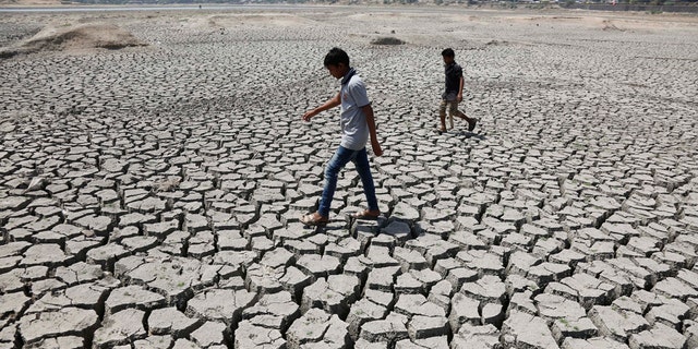 FILE - In this May 14, 2016, file photo, boys on their way to play cricket walk through a dried patch of Chandola Lake in Ahmadabad, India. The decade that just ended was by far the hottest ever measured on Earth, capped off by the second-warmest year on record, NASA and the National Oceanic and Atmospheric Administration reported Wednesday, Jan. 15, 2020. (AP Photo/Ajit Solanki, File)