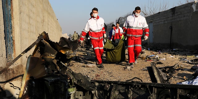 Rescue workers carry the body of a victim of an Ukrainian plane crash among debris of the plane in Shahedshahr, southwest of the capital Tehran, Iran, Wednesday, Jan. 8, 2020. (AP Photo/Ebrahim Noroozi)