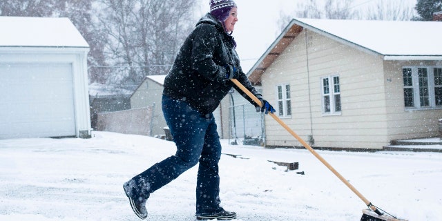 Ashley Reilly sweeps snow from her neighbor's driveway on Wednesday, Jan. 15, in Yakima, Wash.