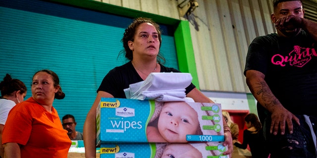A woman carries boxes of baby wipes she removed from a warehouse filled with supplies, including thousands of cases of water, believed to have been from when Hurricane Maria struck the island in 2017 in Ponce, Puerto Rico on Jan. 18, 2020, after a powerful earthquake hit the island. (Photo by Ricardo ARDUENGO / AFP) 