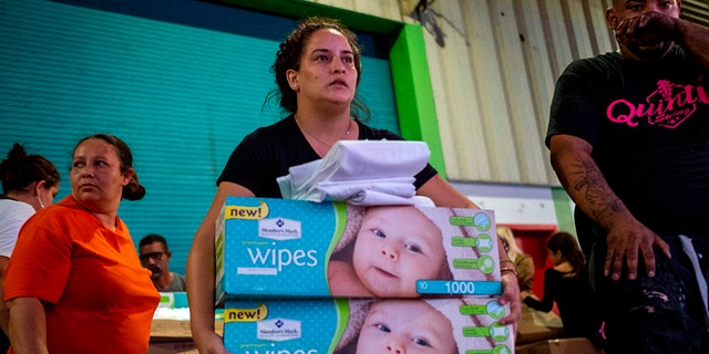 A woman carries boxes of baby wipes she removed from a warehouse filled with supplies, including thousands of cases of water, believed to have been from when Hurricane Maria struck the island in 2017 in Ponce, Puerto Rico on Jan. 18, 2020, after a powerful earthquake hit the island. (Photo by Ricardo ARDUENGO / AFP)