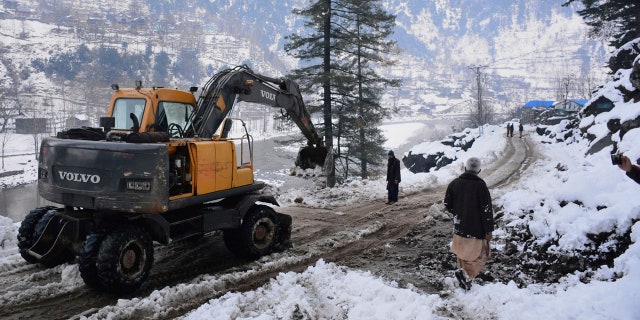 Workers with heavy machinery clear a snow-covered road in Keran, a small town in Neelum Valley, Pakistan-administered Kashmir, Tuesday, Jan. 14, 2020.