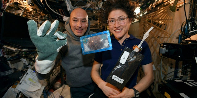 In this photo made available by U.S. astronaut Christina Koch via Twitter on Dec. 26, 2019, she and Italian astronaut Luca Parmitano pose for a photo with a cookie baked on the International Space Station. The results are finally in for the first chocolate chip cookie bake-off in space. While looking more or less normal, the best cookies required two hours of baking time last month up at the International Space Station. It takes far less time on Earth, under 20 minutes. And how do they taste? No one knows. (NASA via AP, File)