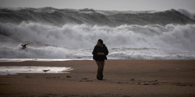 A man walks at the beach during strong winds in Barcelona, Spain, Monday, Jan. 20, 2020.