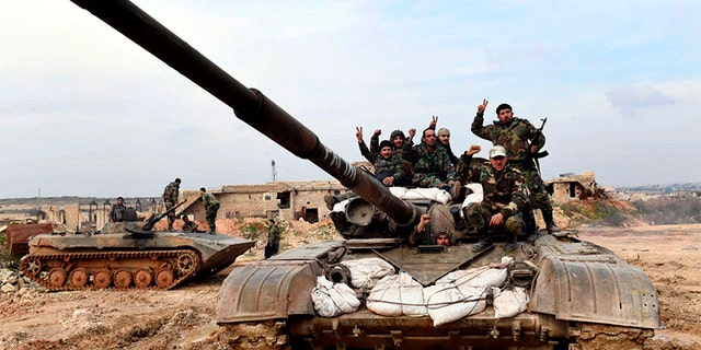 Syrian army soldiers flash the victory sign as they stand on their tank in western rural Aleppo, Syria, on Monday. (AP/SANA)