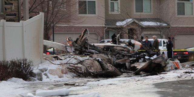 Firefighters and other investigators look at the debris from a small private plane that crashed in a residential area Wednesday, in Roy, Utah. The small plane crashed, killing the pilot as the aircraft narrowly avoided hitting any townhomes, authorities said. (Ben Dorger/Standard-Examiner via AP)