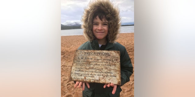 Seven-year-old Patrick McAlindon with a sign from a crate of incendiary bombs he found on a beach at Loch Morlich in the Scottish Highlands on Christmas Day. After just 15 minutes of scanning the beach at Loch Morlich Patrick was stunned when his new gadget showed an “off the scale” reading. (Credit: SWNS)